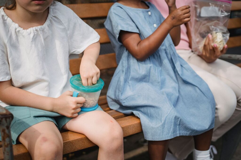 pexels photo 5274691 Children sitting together on a wooden bench, enjoying healthy snacks outdoors.